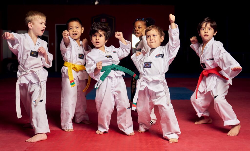 A diverse group of junior martial arts students in white uniforms performing a powerful kihap shout during their martial arts for kids session to build self confidence.