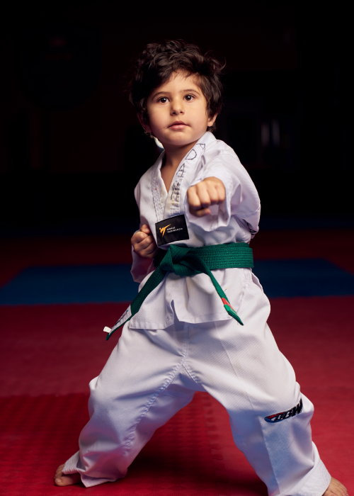 A young green belt student in a solid stance practicing a lead hand punch to improve striking accuracy.