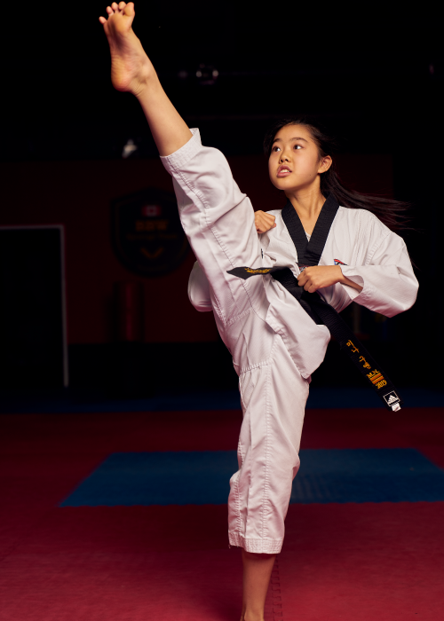 Dedicated young girl performing a professional high kick during a youth martial arts training session.