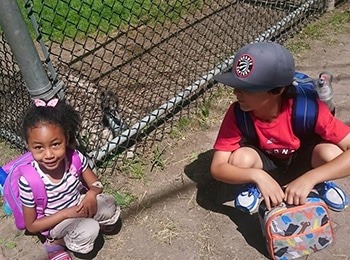 Two young students taking a break during a martial arts youth camp to enjoy a healthy summer camp lunch.