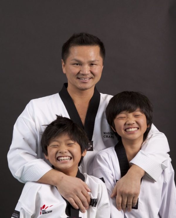 A professional martial arts instructor posing with two young students, demonstrating the strong family atmosphere and positive community found within the dojang.